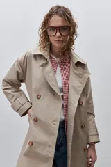 Trench clásico de silueta relajada, color beige, confeccionado en tejido liviano con cuello de solapas, doble abotonadura frontal con botones carey, mangas con presillas regulables y bolsillos laterales funcionales.