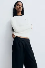 Buzo de punto trenzado color blanco, con cuello redondo, manga larga y un pequeño corazón bordado en el pecho. Presenta terminaciones acanaladas en cuello, puños y ruedo.