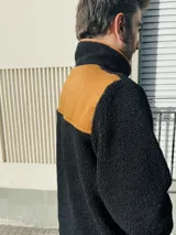 Buzo de hombre de polar negro con cierre parcial color naranja, bolsillo de parche color naranja en la parte inferior y cuello alto.