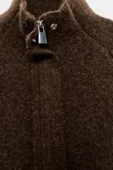 Chaqueta de punto marrón de textura bouclé, con cuello subido, manga larga ancha y cierre frontal oculto con cremallera.