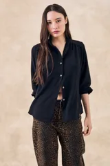 Blusa negra con cuello mao, calce al cuerpo y mangas 3/4 con puños abotonados. Cierre frontal con botones.