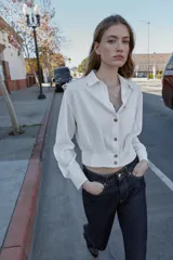 Camisa corta de cuello solapa y manga larga, con trabillas decorativas en los hombros. Presenta pliegues delanteros, elástico en la espalda y cierre frontal con botones.