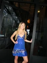 Vestido corto de tela metalizada en tono fucsia con reflejos dorados, con escote en V, diseño de top con triángulos, aberturas laterales en la cintura y doble volado irregular en el ruedo.