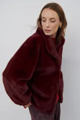 Chaqueta de piel sintética en color burdeos, con cuello alto y cierre frontal oculto. Presenta un diseño de corte recto y mangas largas con puños ligeramente ajustados.