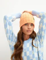 Gorro de lana tejido con punto acanalado, color salmón, con pequeño parche cuadrado con logo en el frente.