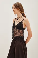 Top de encaje color beige con diseño floral, escote en V y breteles finos. Presenta detalles de bordado con pequeñas cuentas brillantes y terminación con festones en el ruedo.