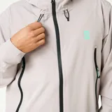 Campera técnica con capucha, color gris claro, con cierre frontal y bolsillos laterales con cremallera. Presenta detalles en color turquesa en los tiradores y logo en el pecho.