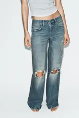 Jeans de tiro medio con diseño flare, efecto lavado y detalles de roturas en las piernas. Presenta cinco bolsillos, trabillas para cinturón y bajo deshilachado sin costuras.