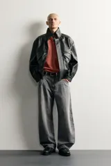 Cazadora relaxed fit de tejido efecto piel en color negro, con cuello subido, manga larga, bolsillos con solapa en el delantero y acabados elásticos. Cierre frontal con cremallera oculta por solapa.