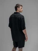 Camisa de corte oversize color negro, confeccionada en lino, con cuello tipo cubano, cierre frontal de botones y mangas cortas.