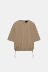 Top de nylon color tostado, con cuello redondo, mangas cortas y bajo abullonado ajustable con cordón y stoppers. Presenta cierre en la espalda con botón.