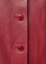 Chaqueta corta de cuero color rojo con cuello camisero blanco, cierre frontal con botones y mangas largas.