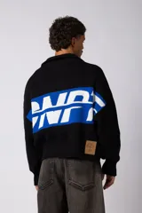 Campera tejida de punto con cierre frontal completo y cuello polo. Presenta un diseño con franja horizontal en color azul y letras en blanco sobre fondo negro, con puños y ruedo acanalados.