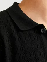 Polo de tejido estructurado negro, con hombros caídos, ajuste holgado, cuello tipo polo, mangas cortas y cierre frontal con botones.