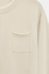 Chaqueta de punto efecto doble capa color beige, con cuello redondo, manga larga y cierre frontal con botones. Cuenta con un bolsillo de plastrón en el pecho y bajo acabado en rib.
