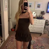 Vestido corto marrón oscuro, estilo strapless, con detalle de frunces en la cintura y falda con volados superpuestos. Incluye un accesorio tipo choker o corbatín a juego.