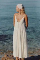 Vestido largo satinado color crudo, con escote en pico adornado con lazada y tirantes finos ajustables. Presenta detalles de frunces y diseño fluido.