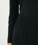 Conjunto de pijama negro de dos piezas, compuesto por una blusa de manga larga con escote en V y detalle de encaje blanco, y un pantalón largo de corte recto con cintura elástica.