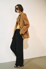 Pantalón de tiro medio color negro con trabillas en la cintura, bolsillos laterales ocultos y pierna recta. Cierre frontal con cremallera, botón y ganchos metálicos.