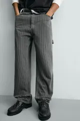 Pantalón de corte ancho (baggy fit) color verde oscuro/gris oscuro con finas rayas verticales blancas. Presenta cintura ajustable con trabillas laterales, bolsillos delanteros, bolsillos traseros de plastrón, bolsillo cerillero y una tira multifunción en la pernera.