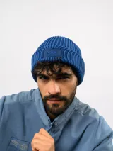 Gorro tipo beanie de tejido acanalado en color azul, con parche rectangular rojo en el frente que presenta el logo de la marca Umbro bordado en blanco.