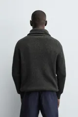 Chaqueta de punto con textura acanalada, cuello subido y cierre frontal completo con cremallera metálica. Presenta un corte relajado y acabados en rib en puños y ruedo.