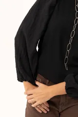 Blusa negra de tejido acanalado con mangas largas abullonadas de textura arrugada y puños elásticos.