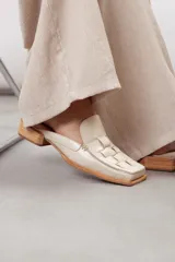 Zueco de cuero vacuno color off-white con diseño texturizado, puntera cuadrada y detalle central de cuero entrelazado. Posee suela y taco bajo de madera clara.
