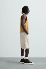 Bermuda de algodón color beige claro con efecto lavado y estampado abstracto en tonos grises. Diseño de corte relajado con cierre frontal de botón y cremallera, bolsillos delanteros y bolsillos traseros de plastrón.