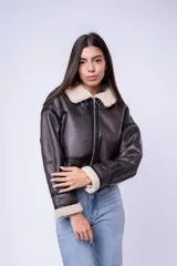 Campera tipo gamulán de cuero sintético marrón oscuro con interior y detalles de corderito sintético en cuello y puños. Presenta cierre frontal, bolsillos laterales con cierre y correas ajustables en el cuello.