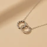 Collar de plata 925 compuesto por una cadena fina de eslabones y un dije formado por dos aros entrelazados, uno de superficie lisa y otro con diseño trenzado.