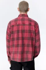 Camisa de sarga de algodón con diseño a cuadros, cuello inglés, bolsillo en el pecho y cierre frontal de botones. Presenta mangas largas con puños abotonados y bajo redondeado.