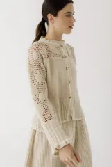 Saco de punto color beige, con diseño de calados en la parte superior y mangas, cierre frontal con botones y cuello redondo.