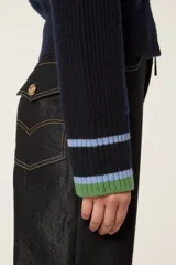 Cárdigan de punto azul marino con cierre frontal de cremallera. Presenta cuello tipo camionero y puños con detalles de rayas en tonos verde y celeste. El tejido tiene una textura acanalada con detalles calados decorativos.