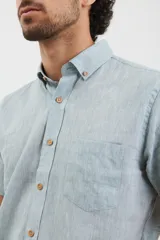 Camisa azul de manga corta, con cuello abotonado y bolsillo en el pecho.