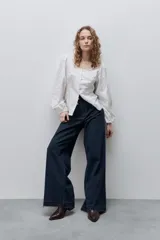 Jean wide leg negro de tiro alto, confeccionado en denim rígido, con diseño de cinco bolsillos, presillas para cinto, cierre frontal con botón y ruedo desflecado.