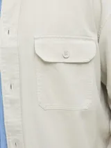 Sobrecamisa de manga larga confeccionada en sarga de algodón, con cuello camisero, cierre frontal de botones y un bolsillo en el pecho. Presenta un corte amplio y estructura versátil ideal para usar como capa ligera.