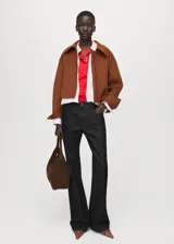 Chaqueta marrón de corte corto y diseño estructurado, con cuello solapa, cierre frontal de cremallera y mangas largas con puños anchos.