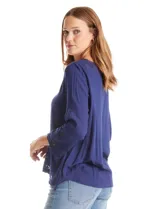 Blusa azul de escote en V y manga larga con terminación amplia. Presenta detalles de bordado y calados tanto en las mangas como en el ruedo delantero.