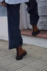 Bota corta de cuero color marrón con paneles en gamuza al tono, diseño de punta redondeada y suela track negra de goma. Presenta cierre lateral y detalle de costuras a la vista.