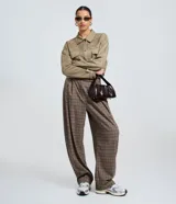 Pantalón de vestir de corte barrel, tiro alto con pliegues delanteros y pierna ancha, confeccionado en tejido con estampado de cuadros en tonos marrones y rojizos.