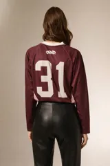 Remera de manga larga estilo deportivo, confeccionada en tejido técnico. Presenta un diseño color block en tonos bordó y rosa, con cuello mao y estampado gráfico frontal en color blanco.