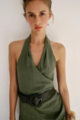 Vestido midi verde militar de cuello halter con escote en V cruzado y espalda descubierta. Cuenta con pliegues laterales, bajo asimétrico y un cinturón incorporado con hebilla redonda oscura.