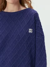 Sweater de cuello redondo con diseño de tejido en relieve de rombos, manga larga y calce holgado. Presenta logo bordado en el pecho y aberturas laterales en el ruedo.