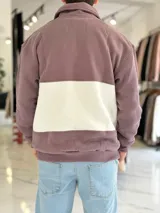 Buzo de algodón negro con una franja horizontal blanca en el centro, cuello solapa con medio cierre y puños y cintura elásticos acanalados. Cuenta con pequeños estampados en el pecho.