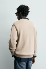 Sweater de punto color beige, de corte regular fit, con cuello redondo y manga larga. Presenta terminaciones en rib en cuello, puños y dobladillo.