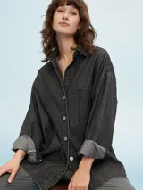 Camisa de denim azul de corte oversize, con mangas largas, cuello clásico, un bolsillo aplicado en el pecho y cierre frontal con botones metálicos.