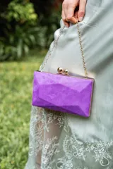 Clutch de gamuza color obispo (morado) con bordes dorados y cadena dorada.