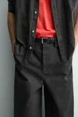 Pantalón de corte relajado confeccionado en tejido de algodón. Presenta cintura con trabillas laterales ajustables, bolsillos frontales y traseros, y un diseño distintivo de costuras laterales giradas que recorren la pernera.
