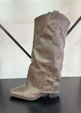 Botas texanas de caña alta color marrón con detalles de tachas doradas. El calzado presenta un diseño con puntera en punta y un pequeño taco cuadrado. Se recomienda pedir un talle más del que se usa habitualmente.